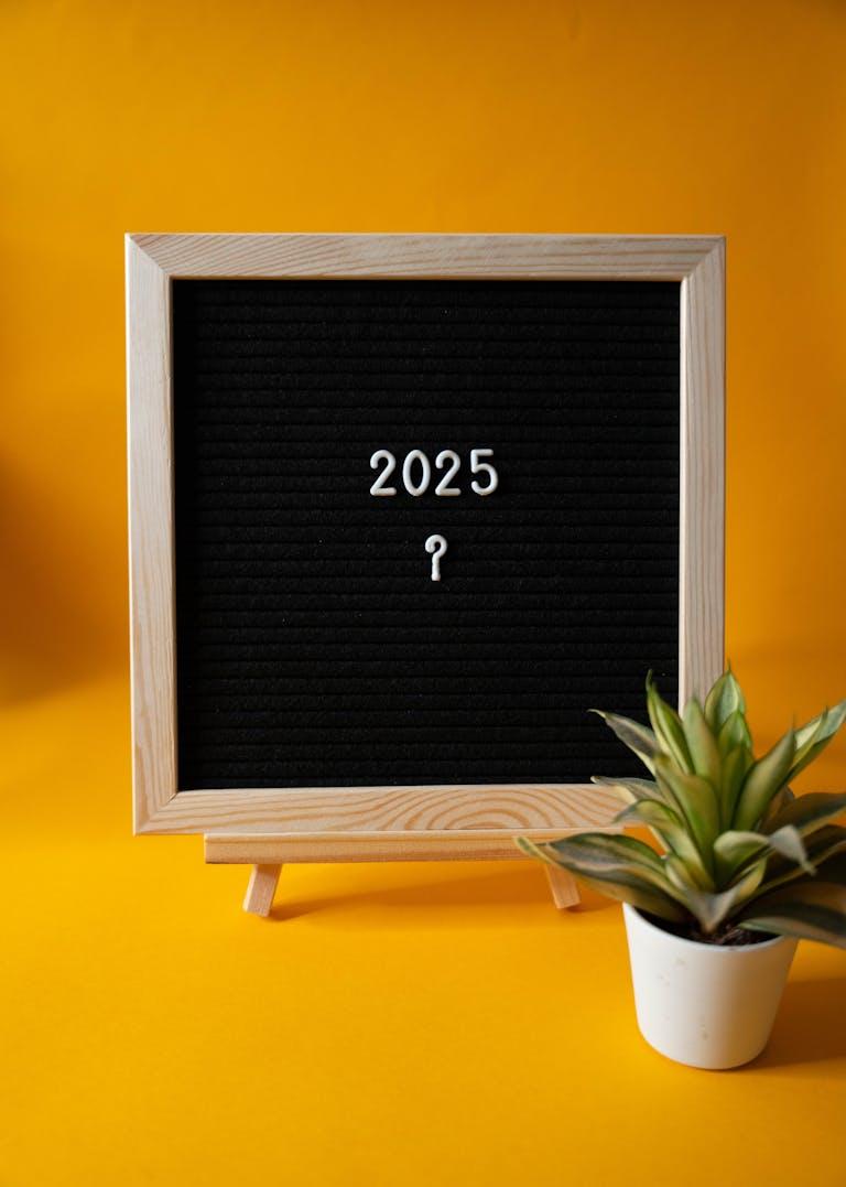 Black letter board displaying '2025' on yellow background with a succulent plant.