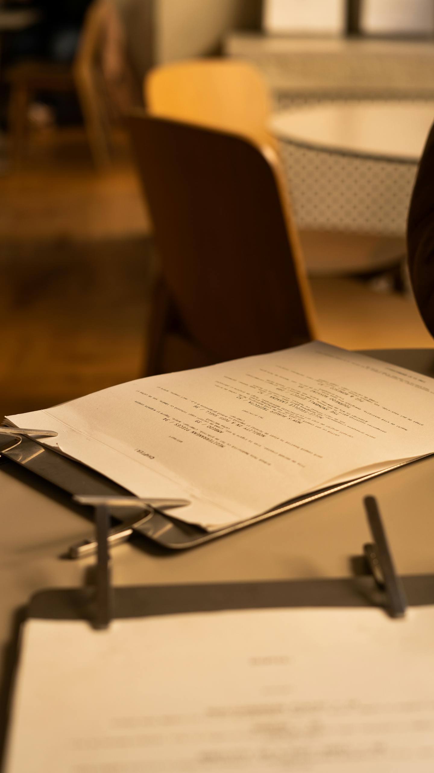 Detailed view of a clipboard with documents in a cozy café environment, offering a warm and inviting atmosphere.